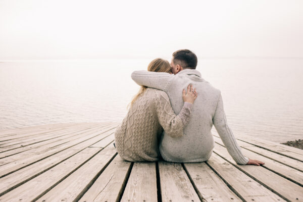 Man and woman sit on the end of a dock with arms around each other