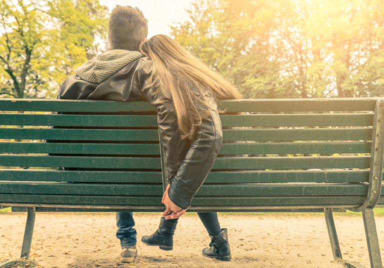 Husband and wife sitting on park bench, color photo