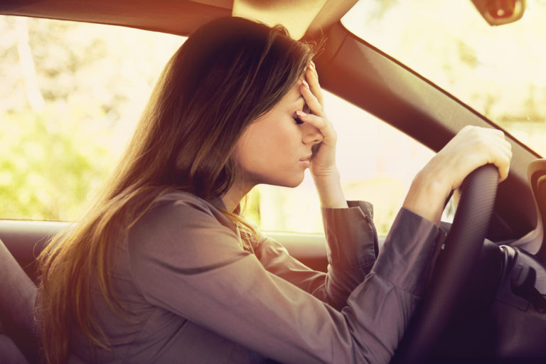 Tired woman with hand on forehead in parked car