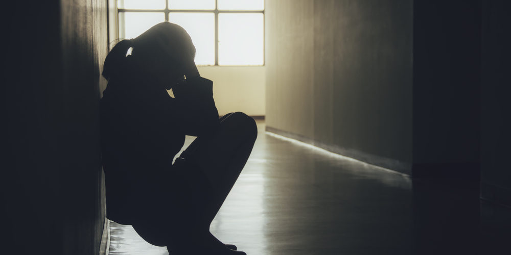 Sad woman head in her hands sitting against a wall