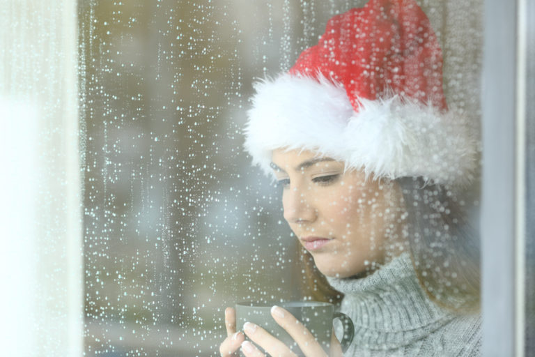 Woman holding coffee cup with Santa hat while looking out window, color photo