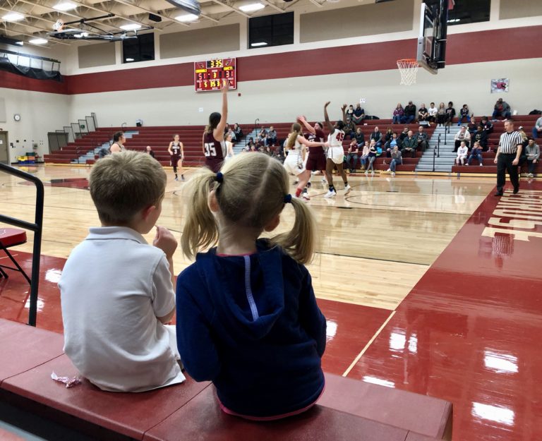 Two young children in the stands of a basketball game watching referees