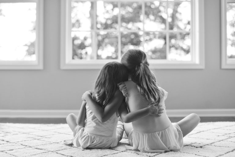 Two young sisters with their arms around each other at home