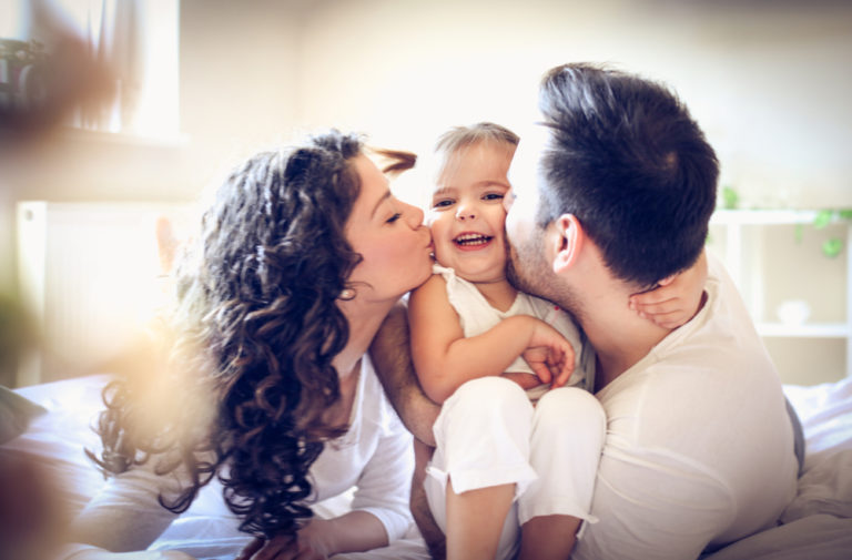 mom and dad holding kissing child between them, color photo