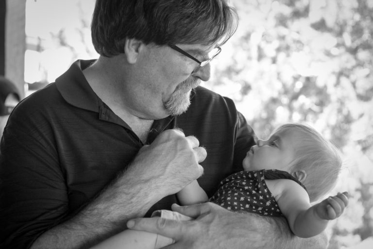 Grandpa holds his infant grandchild and looks at her with love