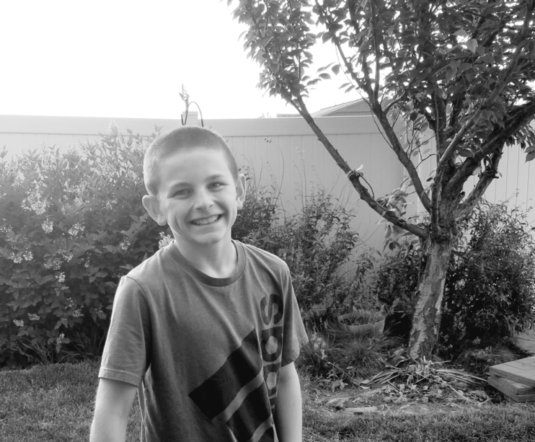 Tween boy holding a ball in the backyard smiling at camera