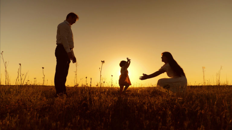 silhouette of toddler walking to mother as father watches