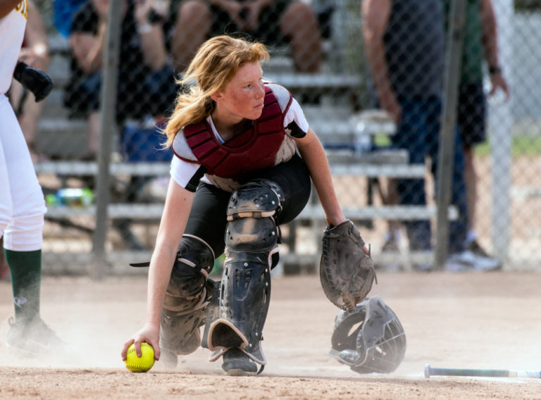 red headed teen girl plays catcher on softball team