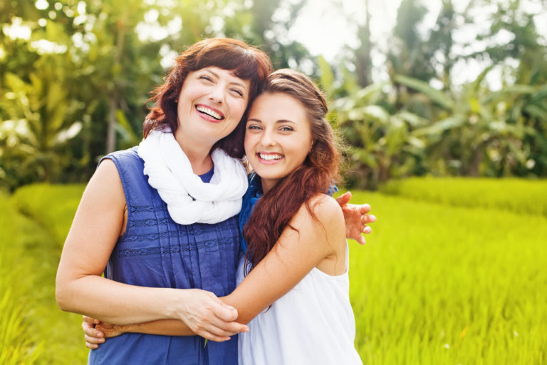 mother and grown daughter smile with arms around each other