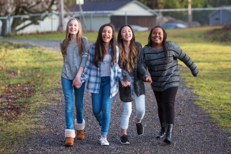 tween girls walk down a path together laughing and holding hands