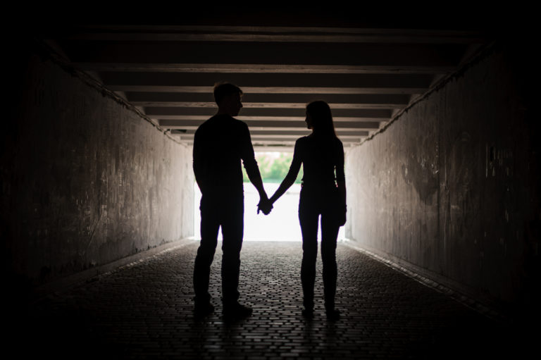 silhouette of man and woman holding hands in a tunnel