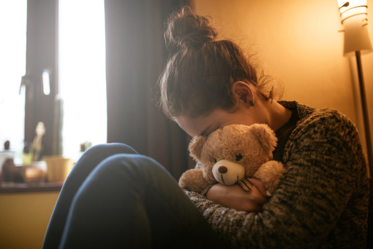 sad woman hides her face in teddy bear after miscarriage