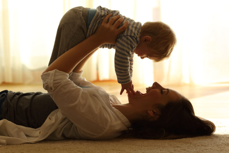 A happy mother lifts her child on the floor at home