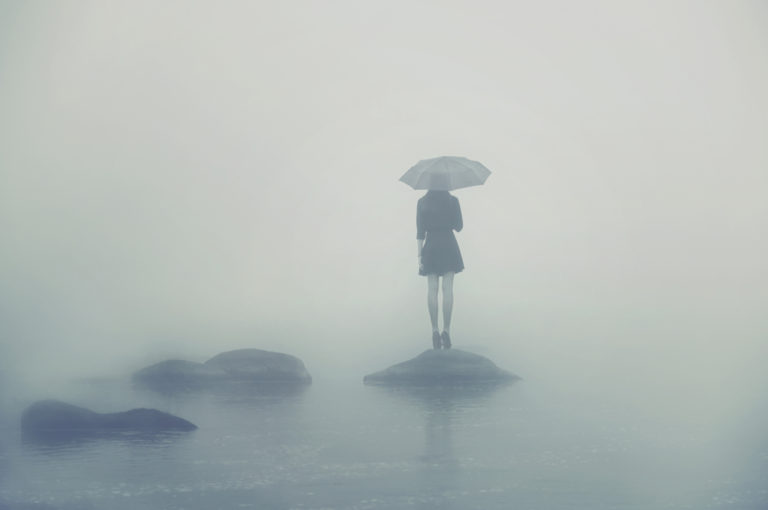 Sad woman stands on a rock in the fog with umbrella