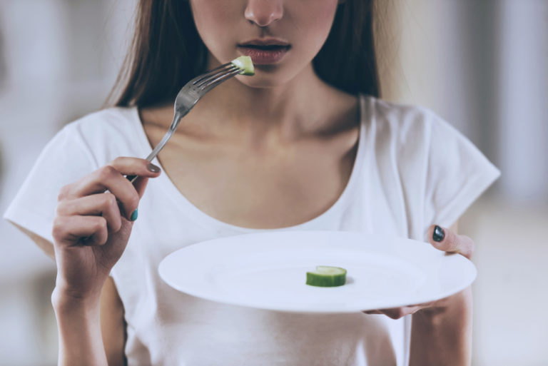 Close up of young girl with anorexia holding plate with vegetable