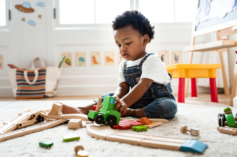 Toddler boy sitting on the floor playing with trains