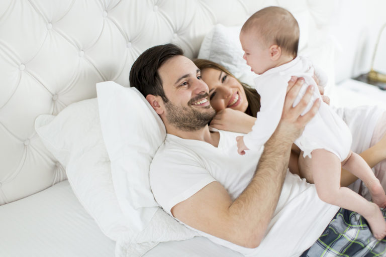 Young couple on bed holding new baby and smiling