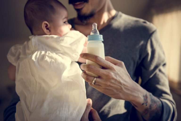 Father holding bottle of milk and infant