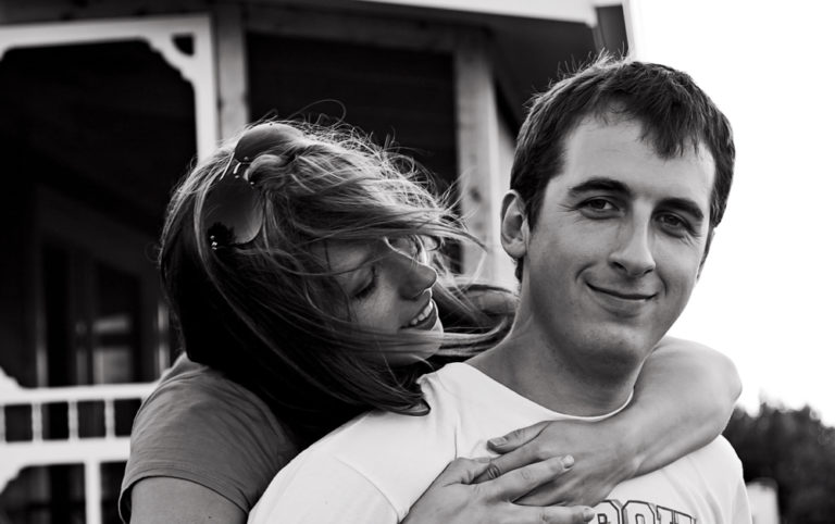 Man smiling at camera with wife hugging him
