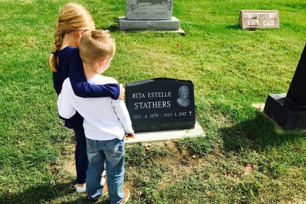Two kids stand beside their grandma's grave