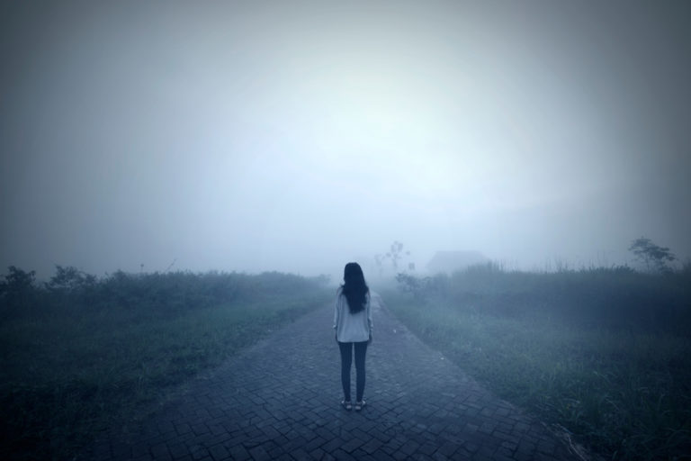 Woman standing in a road alone in the mist