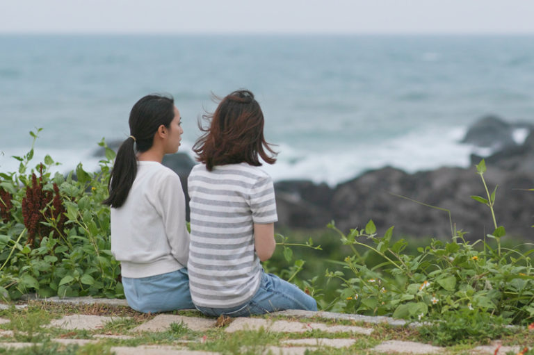 Two women sitting by the ocean