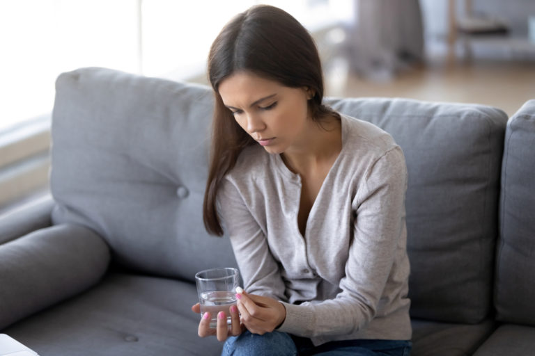 Woman sitting on couch with little white pill and water glass