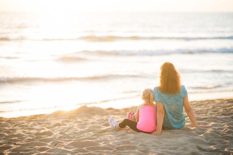Mother and daughter sitting on beach at sunset