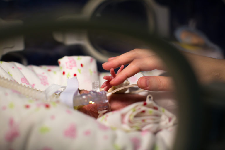 Fragile NICU baby holding mother's hand