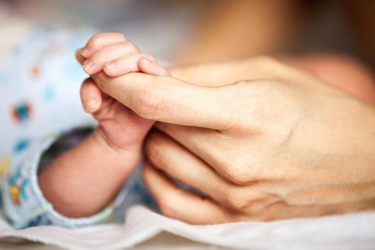 Mother's hand holding baby's fingers