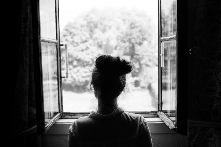 Woman looks out open window
