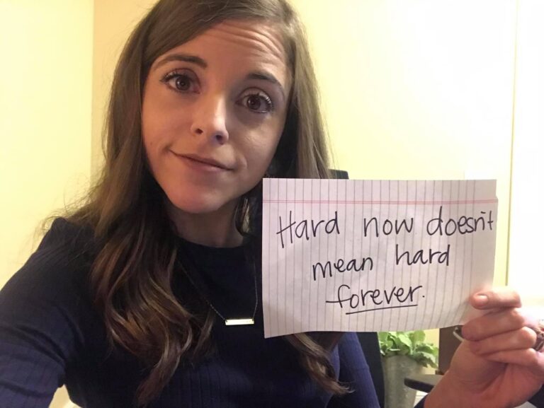 Woman holding paper that reads, "Hard now doesn't mean hard forever," color photo