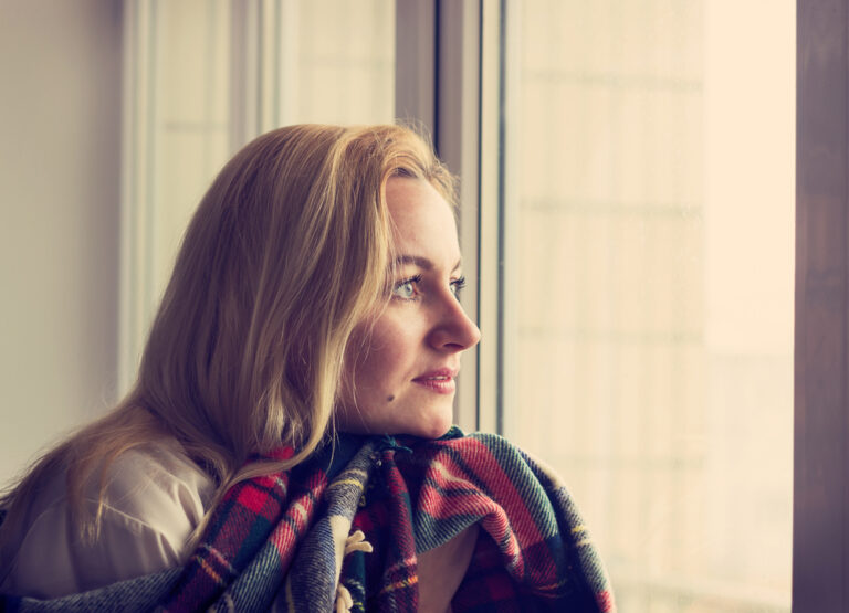 Woman with blanket looking out window
