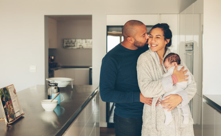 Mother holding baby and father kissing her in kitchen