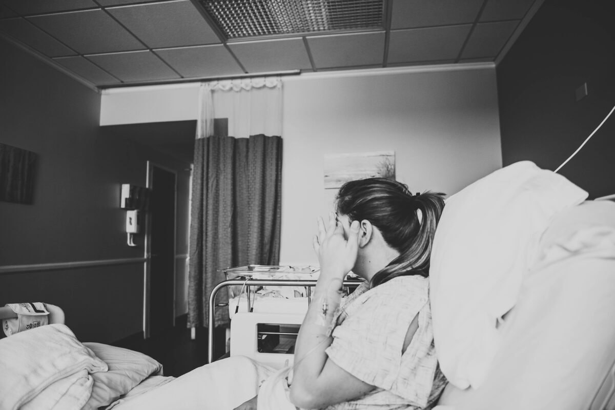 New mom in hospital bed wiping away tear, black and white photo