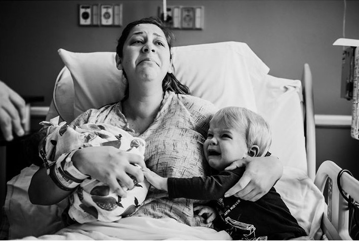 black and white photo of little boy with new baby sister and mom in hospital bed crying