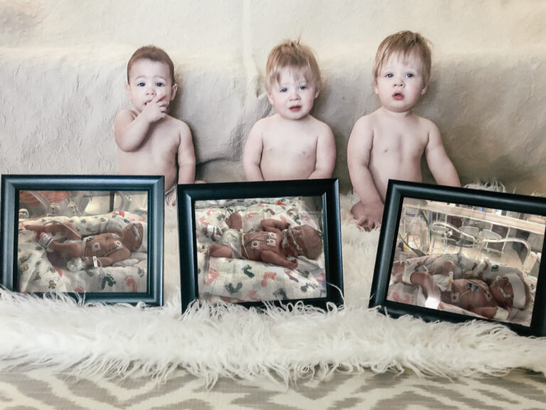One-year-old triplets with their framed newborn pictures, color photo
