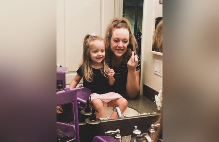 Mother and daughter putting on makeup in bathroom mirror