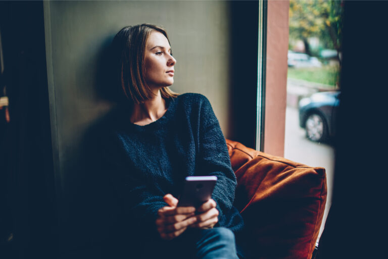 Woman holding coffee and cell phone staring out window