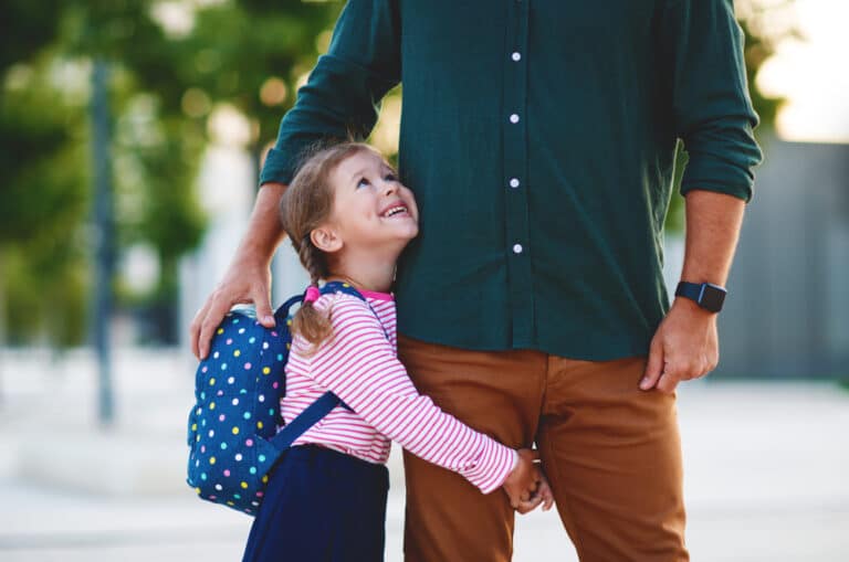 Little girl hugging dad's leg on her way to school