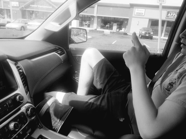 black and white photo of teen on phone in passenger seat of car