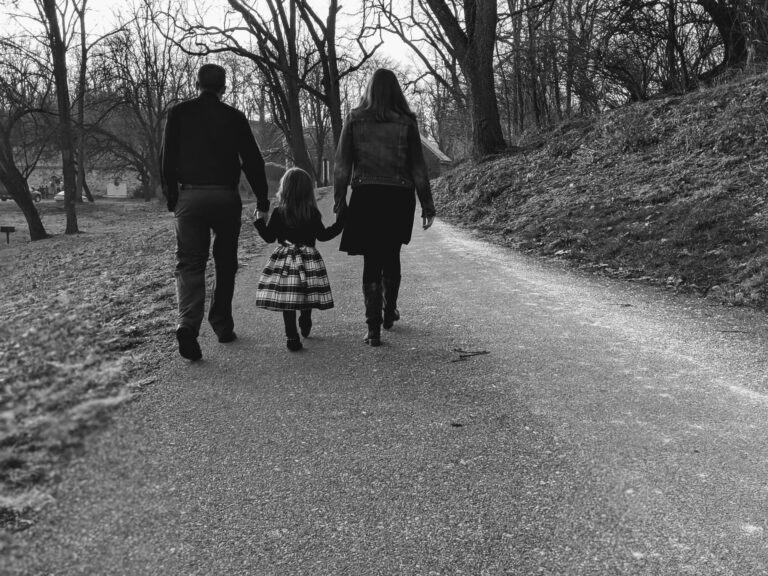 Little girl holding hands and walking with mom and dad on each side, black-and-white photo