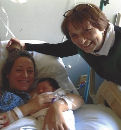 Woman holding newborn baby with grandma smiling by bed