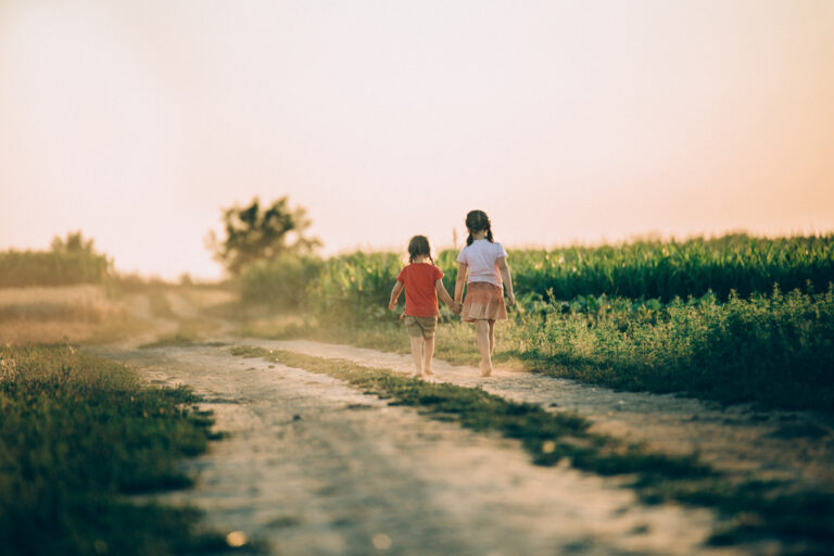Two sisters walking down dirt road at sunset