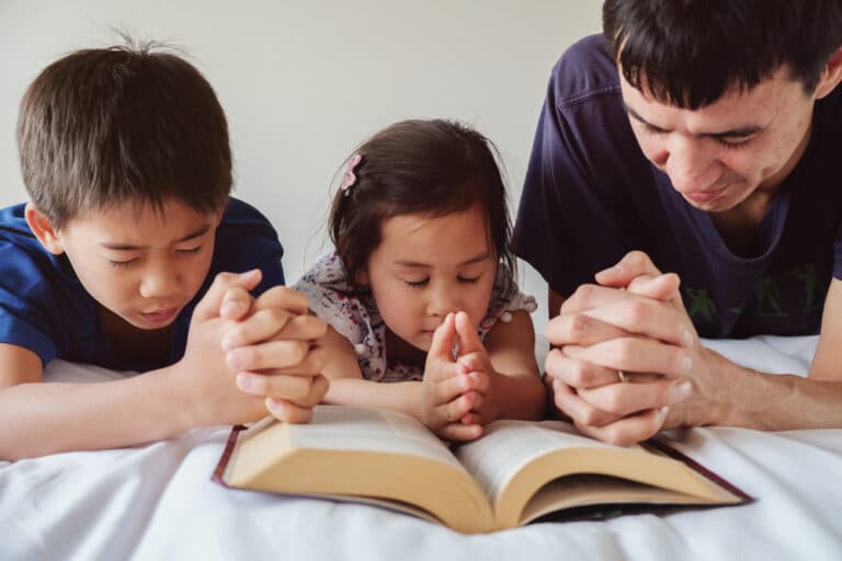 Dad praying with kids and open Bible