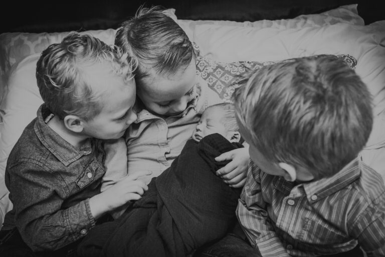 Three big brothers holding and looking on at newborn, black-and-white photo