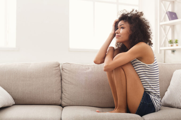Sad woman hugging knees on couch