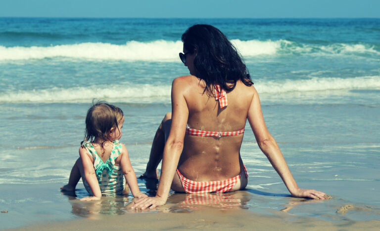 Girl looks at mom on beach and copies pose