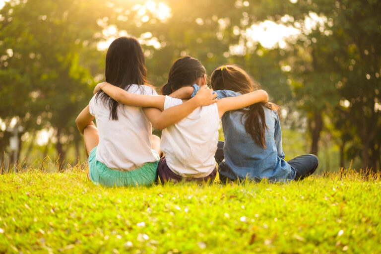 Friends with arms around each other sitting on grass
