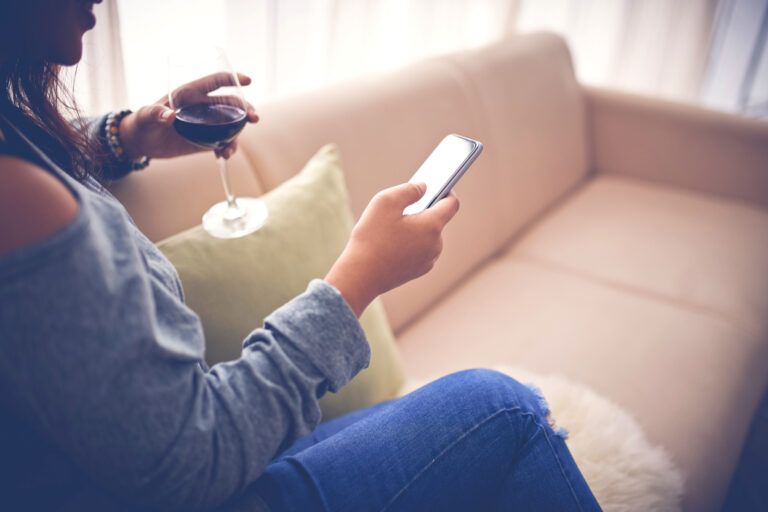 Woman on couch with glass of wine and phone